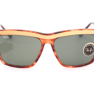 May include: Tortoise shell sunglasses with a gold metal frame and green lenses. The sunglasses have a Ray-Ban logo on the side.