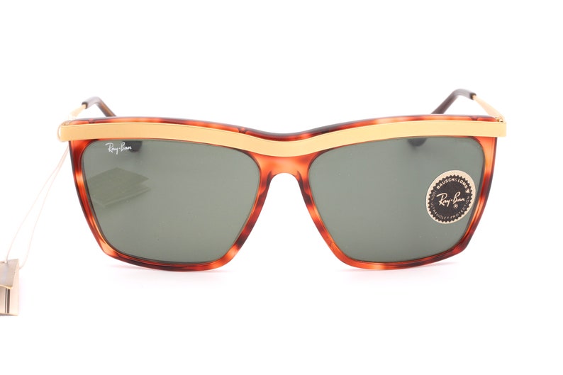 May include: Tortoise shell sunglasses with a gold metal frame and green lenses. The sunglasses have a Ray-Ban logo on the side.