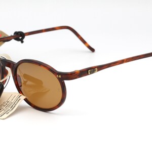 May include: Brown tortoise shell framed sunglasses with brown lenses. The sunglasses have a gold metal logo on the right temple.