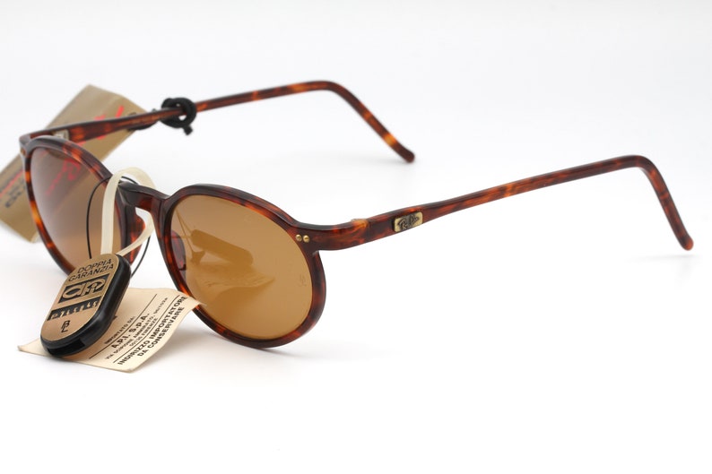 May include: Brown tortoise shell framed sunglasses with brown lenses. The sunglasses have a gold metal logo on the right temple.