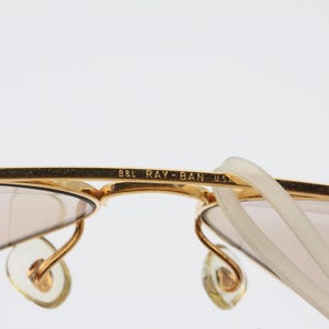 May include: Gold-tone Ray-Ban sunglasses with brown lenses and a B&L Ray-Ban USA inscription on the frame.