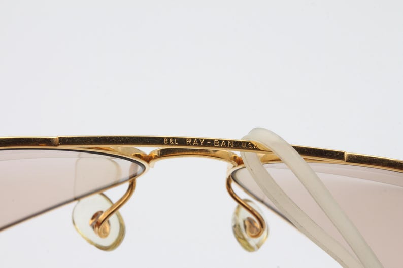 May include: Gold-tone Ray-Ban sunglasses with brown lenses and a B&L Ray-Ban USA inscription on the frame.