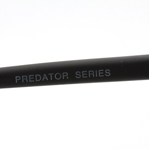 May include: Close-up of the black arm of a pair of glasses with the text "PREDATOR SERIES" printed in white.