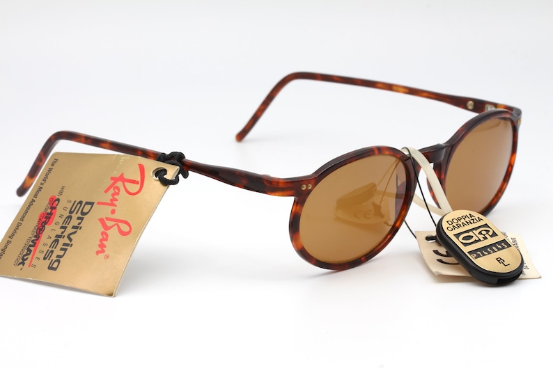 May include: Tortoise shell Ray-Ban Driving Series sunglasses with brown lenses. The sunglasses have a tag attached that reads "Ray-Ban Driving Series Sunglasses CHROMAX".