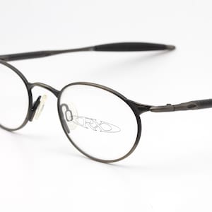 Puede incluir: Un par de gafas de metal negro con lentes redondas. El nombre de la marca "ORXO" es visible en las lentes.