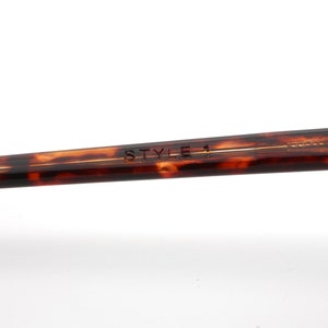 May include: Close-up of the arm of eyeglasses with a tortoiseshell pattern. The text "STYLE 1" is engraved on the arm. A small silver screw is visible near the end of the arm. The glasses are set against a white background.