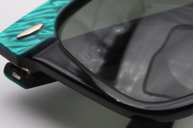 Puede incluir: Primer plano de unas gafas de sol negras y verdes con una montura verde texturizada. Las gafas de sol tienen una montura de pl&aacute;stico negro y lentes verdes. El texto "22" es visible en la lente derecha.