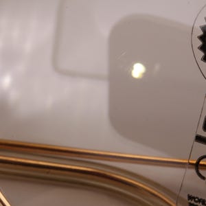 May include: Close-up of a gold-coloured metal frame of a pair of sunglasses with a black and white label that reads "100% UV Sunglasses by Ray-Ban CHANGE"