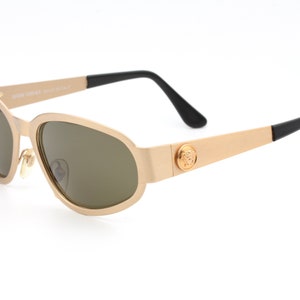 May include: Gold-toned sunglasses with brown lenses and a black Versace logo on the side.