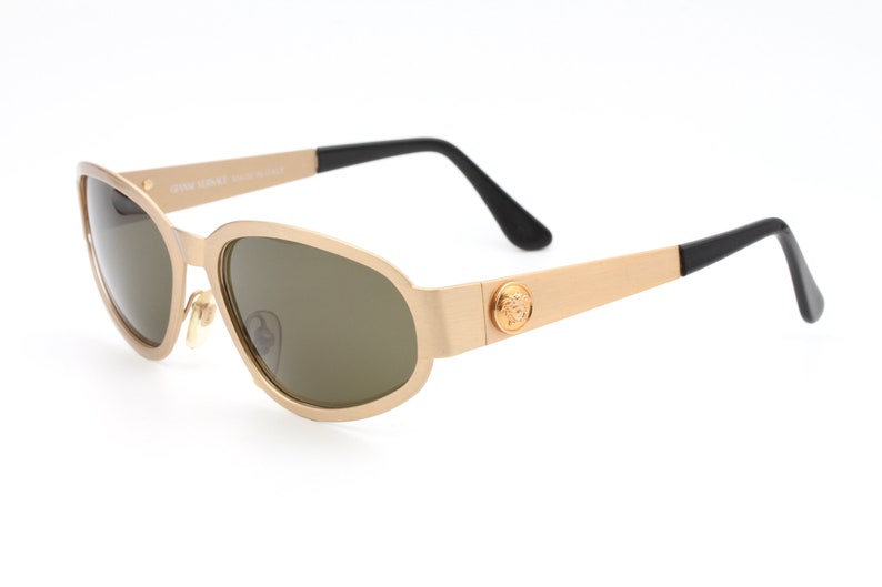 May include: Gold-toned sunglasses with brown lenses and a black Versace logo on the side.