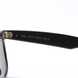 May include: Black Ray-Ban sunglasses with green lenses. The sunglasses have a metal hinge and the text "B&L RAY-BAN U.S.A." is printed on the arm.
