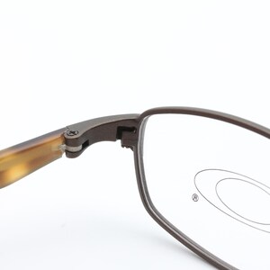 May include: Close-up of Oakley eyeglasses. The frames are a dark brown color with a rectangular shape. The temples have a tortoise shell pattern. The lenses are clear with the Oakley logo visible.