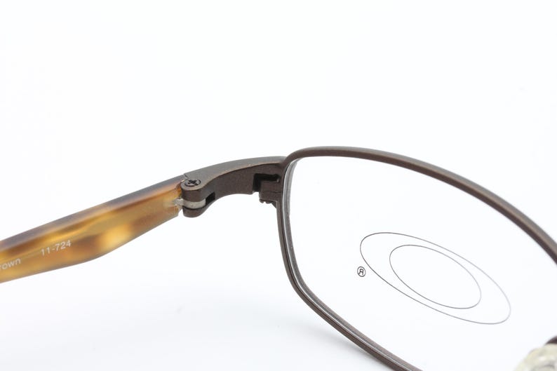May include: Close-up of Oakley eyeglasses. The frames are a dark brown color with a rectangular shape. The temples have a tortoise shell pattern. The lenses are clear with the Oakley logo visible.