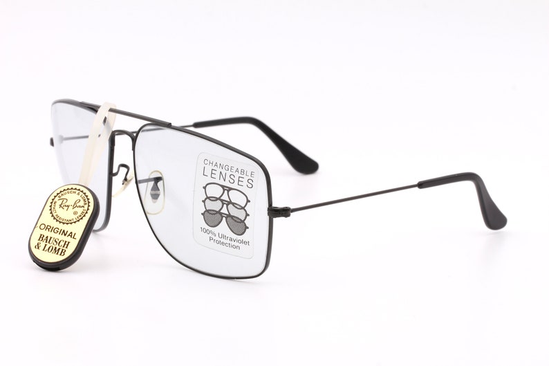 May include: Black rectangular frame glasses with clear lenses. The glasses have a label that says "Changeable Lenses" and "100% Ultraviolet Protection". A small tag attached to the glasses says "Original Bausch & Lomb".