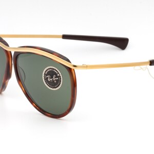 Pu&ograve; includere: Occhiali da sole aviator in tartaruga con dettagli dorati e lenti verdi. Gli occhiali hanno il logo Ray-Ban sulla lente destra.