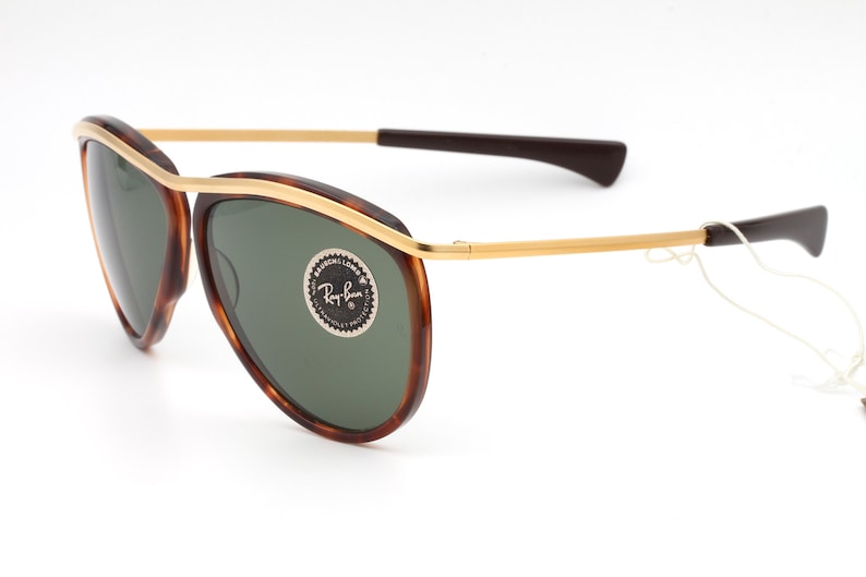Pu&ograve; includere: Occhiali da sole aviator in tartaruga con dettagli dorati e lenti verdi. Gli occhiali hanno il logo Ray-Ban sulla lente destra.
