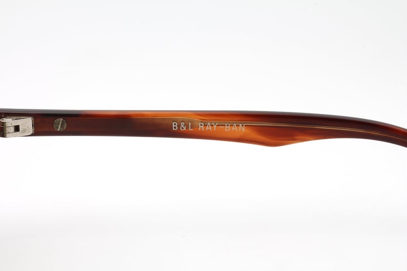 May include: Close-up of the brown tortoise shell frame of a pair of Ray-Ban sunglasses. The frame is engraved with the text "B&L RAY-BAN".