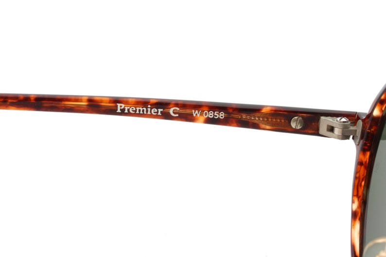 May include: Close-up of the tortoiseshell frame of a pair of sunglasses. The frame has the text "Premier C W 0858" printed on it.