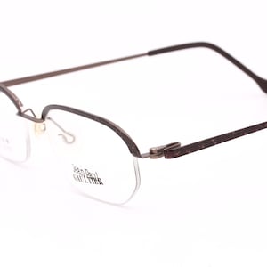 May include: Brown metal frame eyeglasses with a rimless design. The glasses have a Jean Paul Gaultier logo on the right lens.