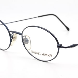 May include: Black metal framed eyeglasses with round lenses and the text "Giorgio Armani" on the right lens.