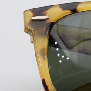 Puede incluir: Primer plano de gafas de sol con montura con estampado de carey. Las lentes son de color verde oscuro y la montura tiene un detalle plateado en la patilla. La marca "B & J" es visible en la lente.