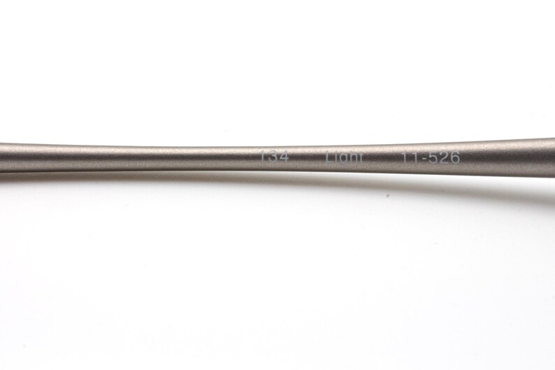 May include: A close-up of a metallic gray object with the text "134 Liont 11-526" printed on it. The object has a smooth, cylindrical shape and is set against a white background.