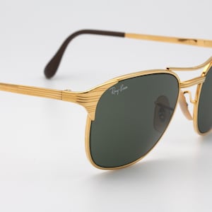 May include: Gold-tone aviator sunglasses with green lenses and a Ray-Ban logo on the frame.