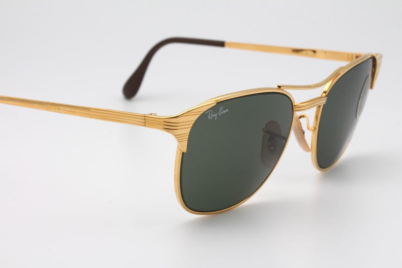 May include: Gold-tone aviator sunglasses with green lenses and a Ray-Ban logo on the frame.