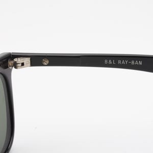 May include: Black Ray-Ban sunglasses with gold accents. The sunglasses have a classic design with a rectangular frame and green lenses. The text "B&L RAY-BAN" is printed on the temple.