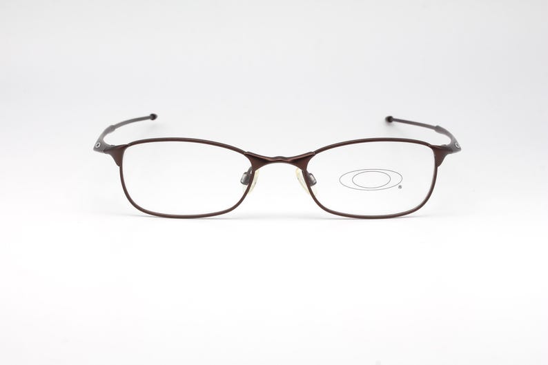 May include: A pair of brown metal eyeglasses with clear lenses. The lenses have a small oval shape in the center.