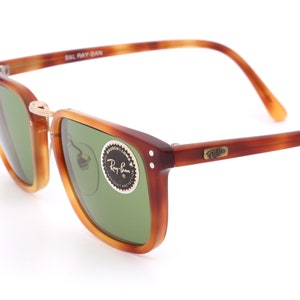 Può includere: Occhiali da sole Ray-Ban in tartaruga con lenti verdi. Gli occhiali hanno una montatura in metallo dorato e il logo Ray-Ban è visibile sulla lente destra.