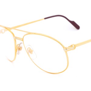 May include: Gold-tone aviator eyeglasses with clear lenses and a thin, burgundy-colored temple arm.