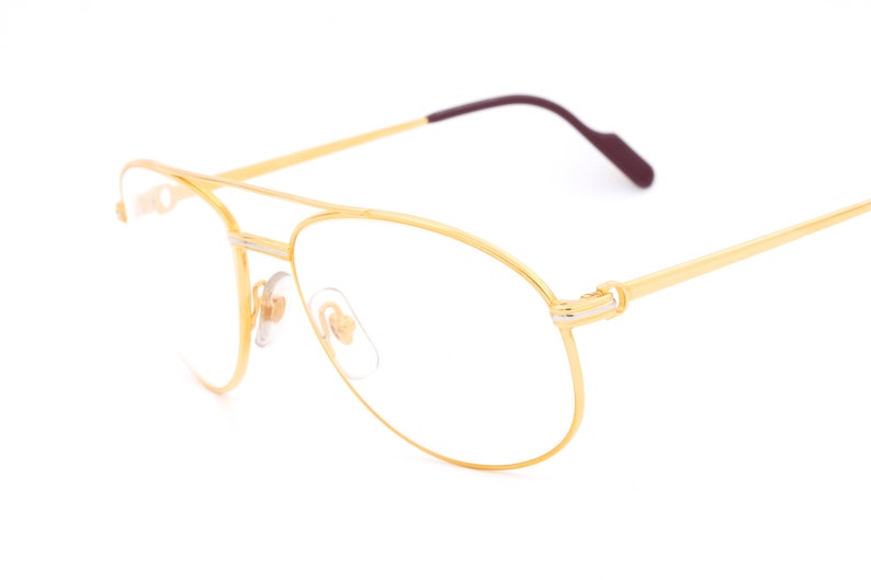 May include: Gold-tone aviator eyeglasses with clear lenses and a thin, burgundy-colored temple arm.