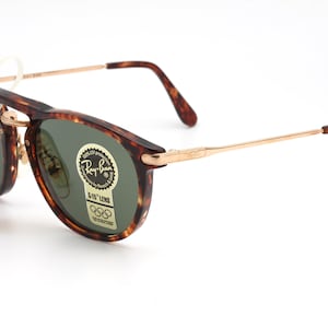 Op de afbeelding: Schildpad Ray-Ban zonnebril met gouden metalen armen en groene lenzen. De zonnebril heeft G-15 lenzen en een Ray-Ban logo sticker op de rechter lens.