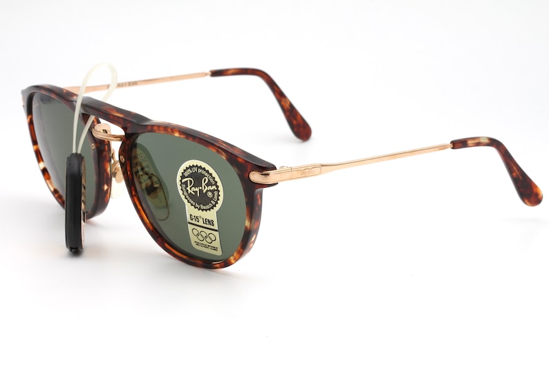 Op de afbeelding: Schildpad Ray-Ban zonnebril met gouden metalen armen en groene lenzen. De zonnebril heeft G-15 lenzen en een Ray-Ban logo sticker op de rechter lens.
