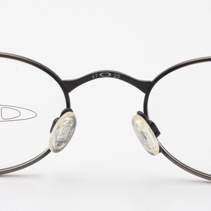 May include: Black round eyeglasses with clear lenses and a silver inscription that reads "47 20" on the bridge.
