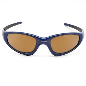 Puede incluir: Un par de gafas de sol azules con lentes marrones. Las gafas tienen un diseño deportivo y envolvente.