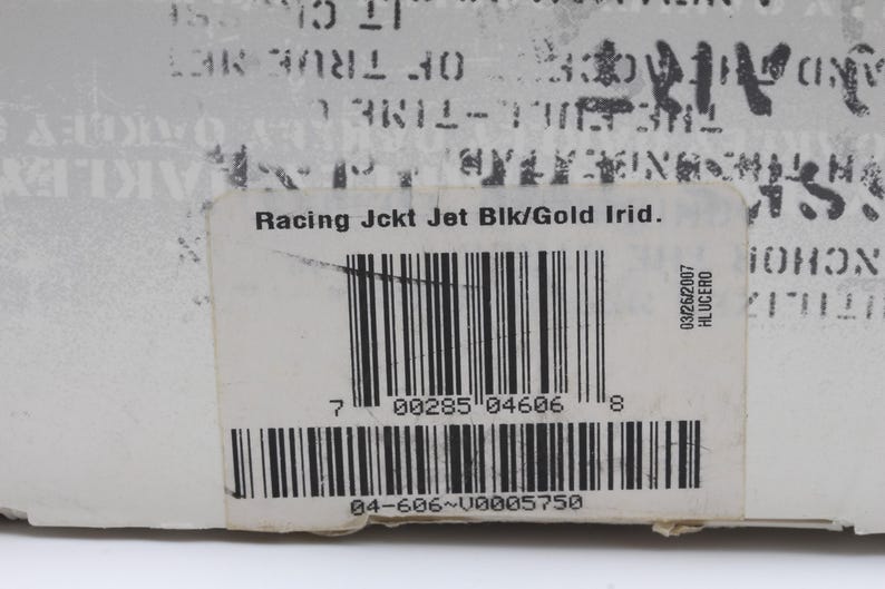 May include: A white label with black text that reads "Racing Jckt Jet Blk/Gold Irid." and a barcode. The barcode number is 00285 04606. The label also has a smaller label with the text "03/26/2007 HLUCERO".