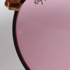 May include: Close-up of the inside of a pink-tinted sunglass lens with a small "B&L" inscription.