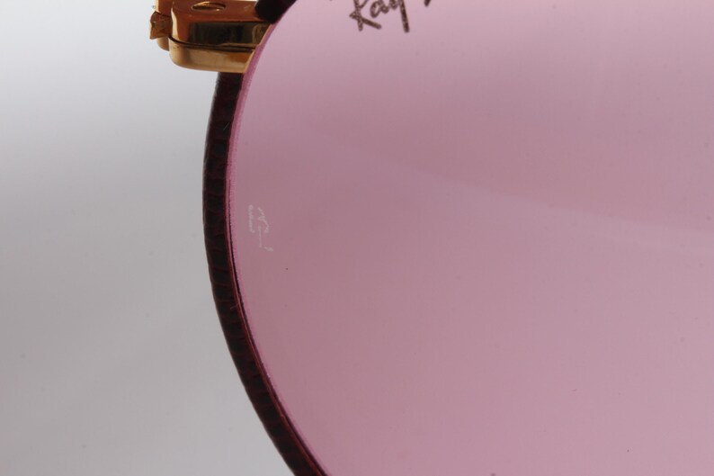 May include: Close-up of the inside of a pink-tinted sunglass lens with a small "B&L" inscription.
