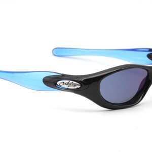 May include: Black and blue Oakley sunglasses with a silver logo. The sunglasses have a curved, wraparound design.