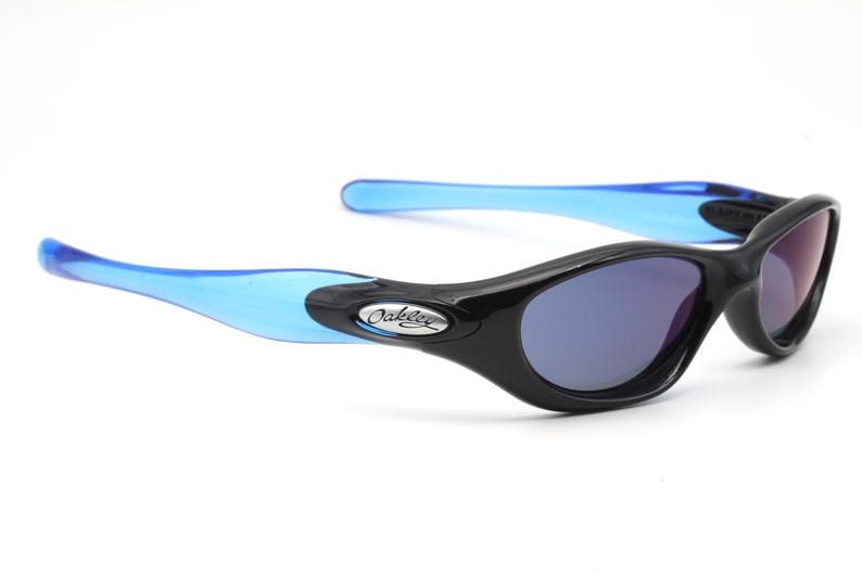 May include: Black and blue Oakley sunglasses with a silver logo. The sunglasses have a curved, wraparound design.