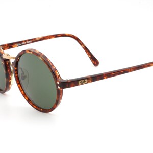 May include: Tortoiseshell round frame sunglasses with green lenses. The sunglasses have a gold metal bridge and the Ray-Ban logo is visible on the right arm.