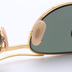 May include: Gold-tone sunglasses with green lenses and a gold metal frame. The sunglasses have a classic aviator style with a thin metal bridge and earpieces.