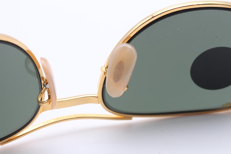 May include: Gold-tone sunglasses with green lenses and a gold metal frame. The sunglasses have a classic aviator style with a thin metal bridge and earpieces.