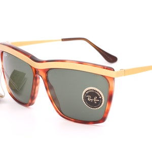May include: Tortoise shell Ray-Ban sunglasses with gold accents and green lenses. The sunglasses have a gold Ray-Ban logo on the right lens.