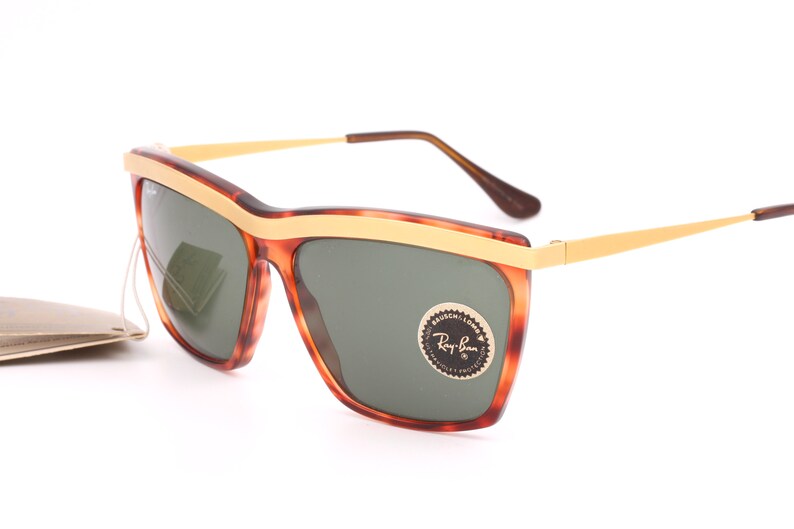 May include: Tortoise shell Ray-Ban sunglasses with gold accents and green lenses. The sunglasses have a gold Ray-Ban logo on the right lens.