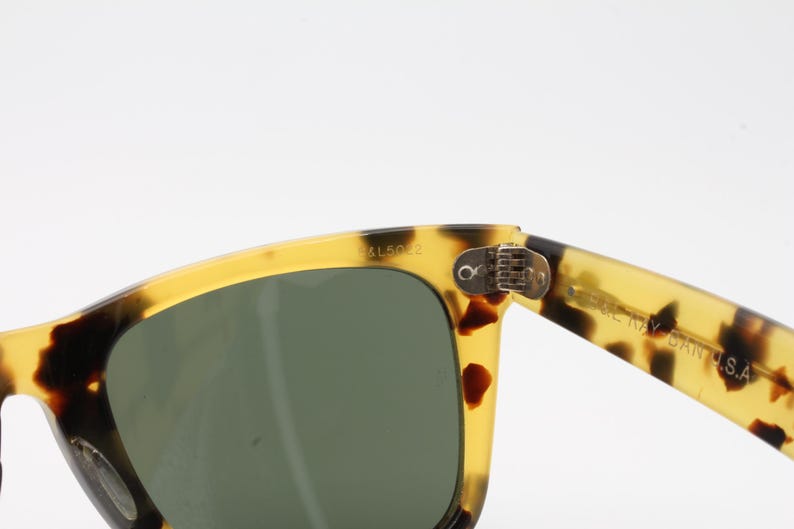 Puede incluir: Primer plano de gafas de sol con montura con estampado de carey y lentes verde oscuro. La montura es una mezcla de amarillo y marr&oacute;n, con el texto "B15022" visible en la esquina superior izquierda. La patilla de las gafas tiene el texto "MADE IN ITALY" y "GAN S.A."