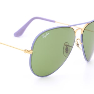 Op de afbeelding: Paarse en gouden aviator zonnebril met groene glazen. De zonnebril heeft het Ray-Ban logo op de rechter lens.