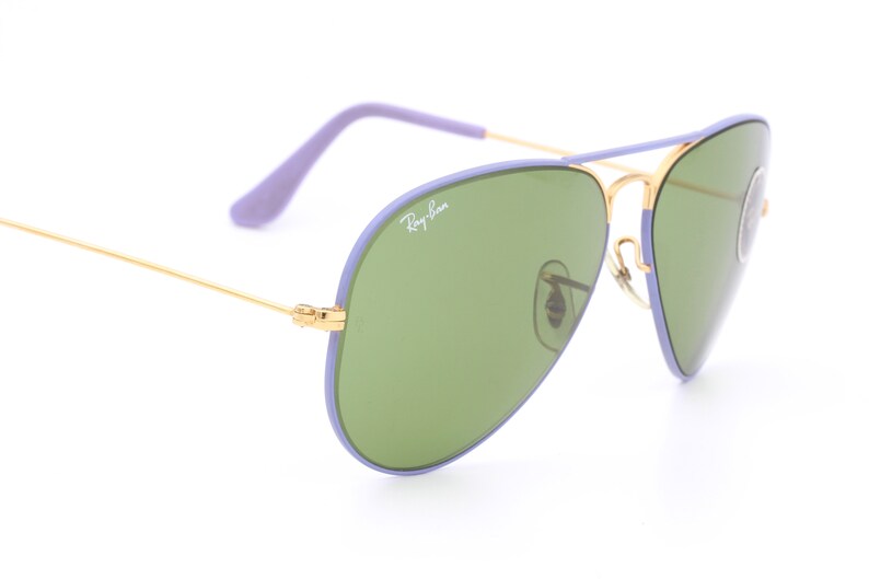 Op de afbeelding: Paarse en gouden aviator zonnebril met groene glazen. De zonnebril heeft het Ray-Ban logo op de rechter lens.